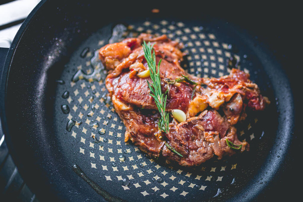 Beef steak with rosemary, garlic, salt and pepper inside iron skillet - Photo, Image