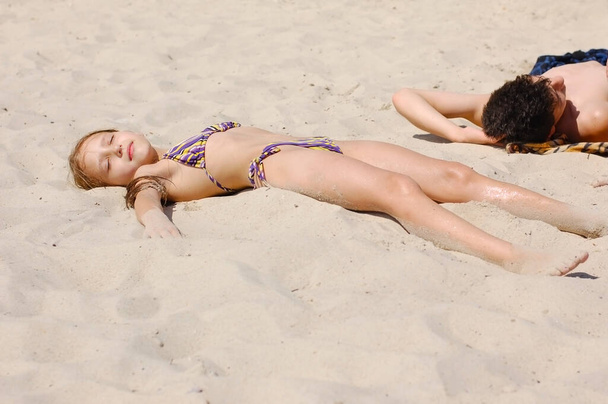 Νεαρό κορίτσι και αγόρι είναι ξαπλωμένοι στην άμμο και κάνουν ηλιοθεραπεία. Τους αρέσει να κάνουν ηλιοθεραπεία και να κολυμπούν στη θάλασσα - Φωτογραφία, εικόνα