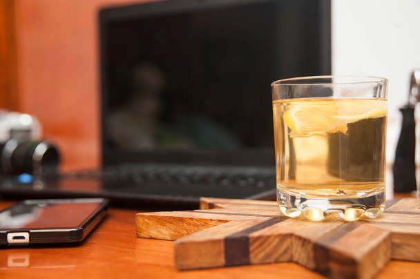 Lahodný čaj s citronem v průhledné sklenici na stole vedle telefonu, notebooku a fotoaparátu - Fotografie, Obrázek