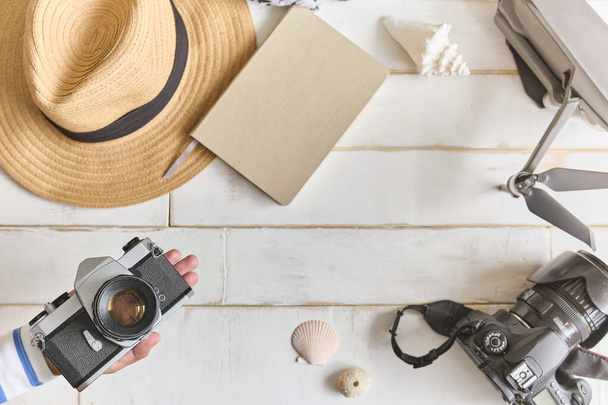 Horní pohled na analogovou kameru a notebook na dřevěném stole, ruce fotografa drží starou filmovou kameru na dřevěném pozadí, cestovní oblečení, koncepce cestování - Fotografie, Obrázek