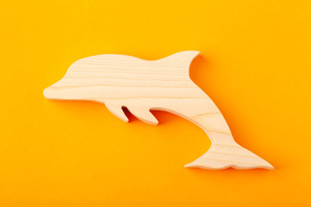 Dolphin figurine carved from solid pine by hand jigsaw. On a yellow background. - Fotografie, Obrázek