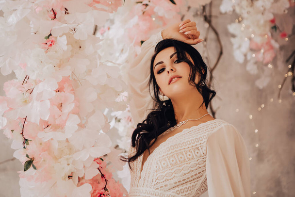 Woman married bride celebrate engagement. Pink wedding photo zone in studio made of white flowers. Place for making pictures. Procreation romantic amazing woman indoor, copy space. - Photo, image