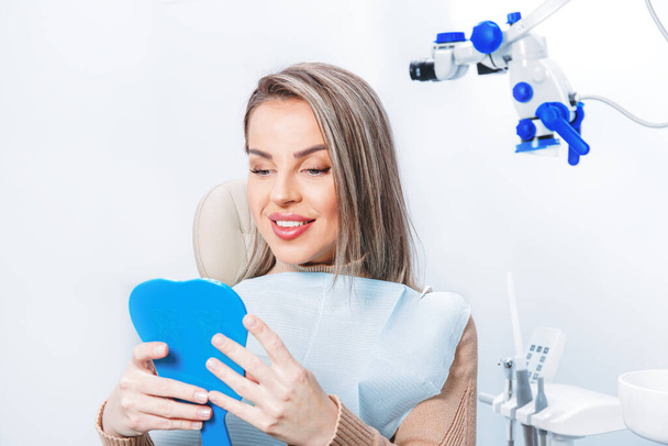 Een vrouw die naar haar tanden kijkt. Glimlachende dame bij de tandarts. Tandarts behandeling, perfecte glimlach - Foto, afbeelding