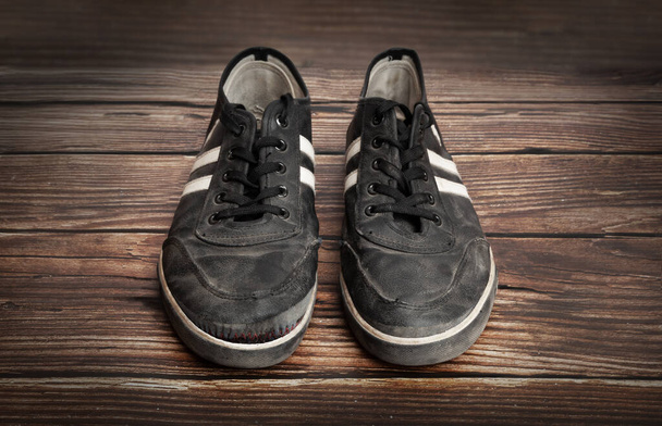 Dirty old black sneakers isolated on a wooden plank background - 写真・画像
