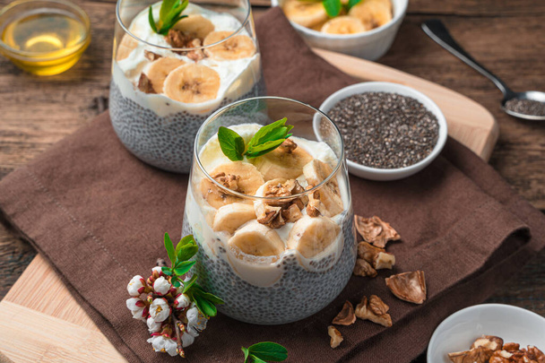 Postre saludable con semillas de chía y leche de coco con plátano, miel y nueces sobre un fondo marrón de madera. - Foto, imagen