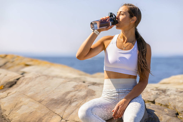 Vrouwelijke atleet Drinkwater tijdens Outdoor Workout by the Sea - Foto, afbeelding