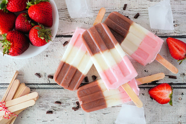 Homemade strawberry vanilla chocolate neapolitan yogurt popsicles. Overhead table scene on a rustic white wood background. - Foto, Imagem