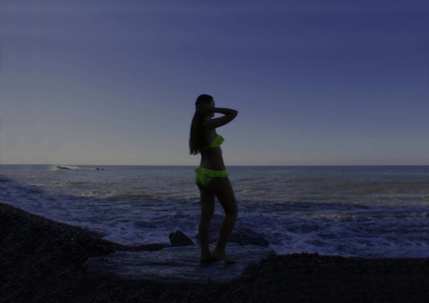 若い女性がビキニ姿で海辺の日陰に立っている。明確な女性的なシルエットではなく、曖昧で明確なシルエットではありません. - 写真・画像