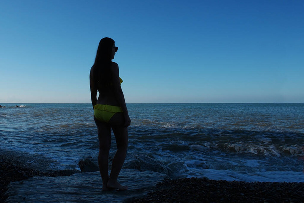 Une jeune femme se tient à l'ombre sur la plage au bord de la mer en bikini. Pas une silhouette féminine claire, une silhouette vague, pas claire. - Photo, image