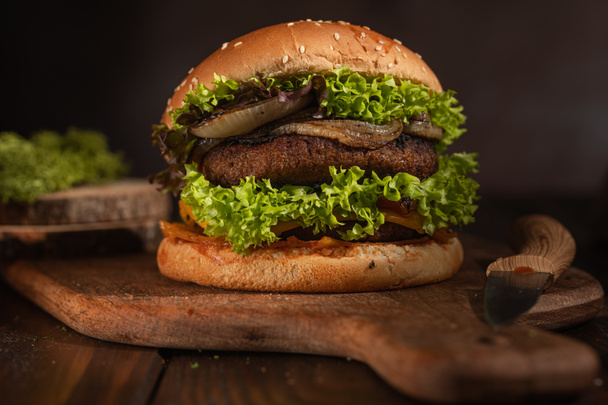 Hamburger z podwójnym wegańskie pea patty, karmelizowana cebula i sałata na desce z mango drewna na ciemnej drewnianej powierzchni - Zdjęcie, obraz