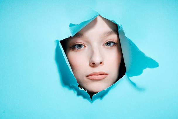 Portrait of a beautiful young girl through a hole in a bright background - Φωτογραφία, εικόνα