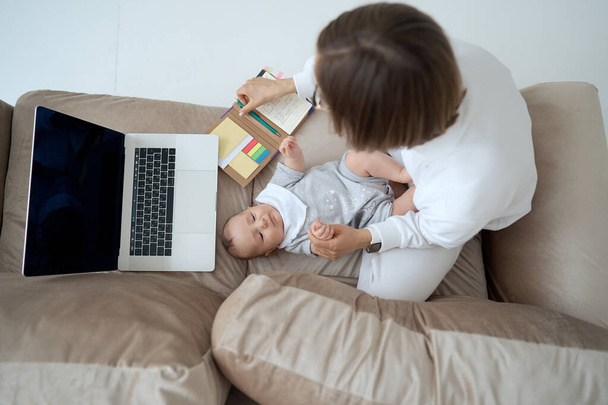 Young mother working on a laptop. Business Woman working from home with little girl. Work on maternity leave. Covid-19. - Fotoğraf, Görsel