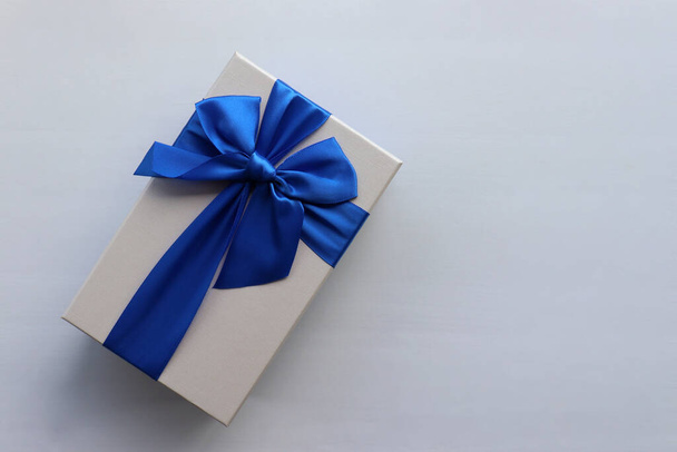 Gift box with blue ribbon on white table background. Fathers day present for dad. Top view, copy space - 写真・画像
