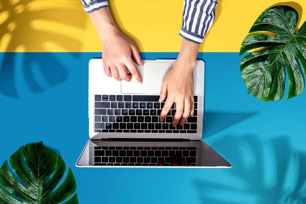 Person using a laptop computer with tropical leaves - Фото, изображение