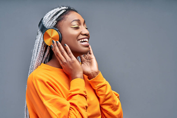 African american woman singing while listening to music on headphones isolated on grey background. Copy space. Side view - Foto, imagen