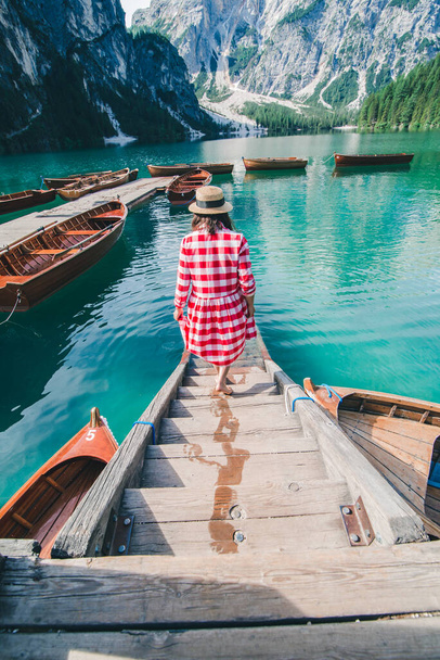 young gentle woman in red checkered dress barefoot walking by wooden stairs of boat station leads to lake - Photo, Image