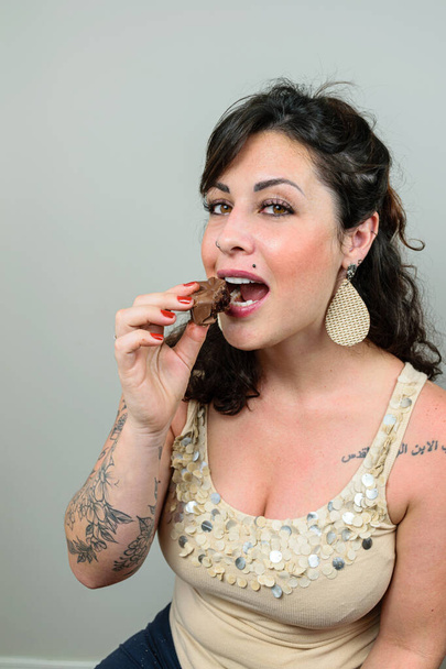 A tetovált nő kamerát keres, készen áll megenni egy brazil méztortát. Tetoválás a bal vállára írva arabul - Apa, Fiú és Szentlélek. - Fotó, kép