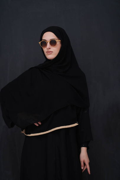 Young muslim in traditional clothes or abaya and sunglasses posing in front of black chalkboard. Arab woman representing modern arabic lifestyle, islamic fashion and Ramadan kareem concept - Foto, Imagem