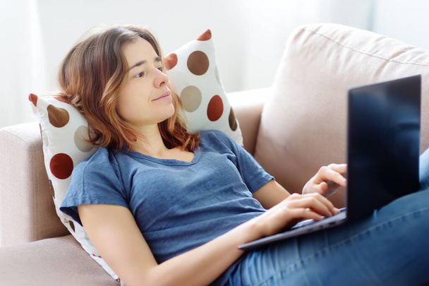 Young woman working with laptop computer lying on sofa at home. Freelancer or blogger. Distance learning of new profession. Additional education. Retraining courses. Business online for adults - Фото, зображення
