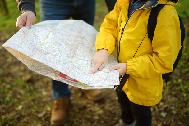 Schoolchild and his mature father hiking together and exploring nature. Little boy with dad looking map during orienteering in forest. Adventure, scouting and hiking tourism for kids. Daddy and son - Foto, Bild