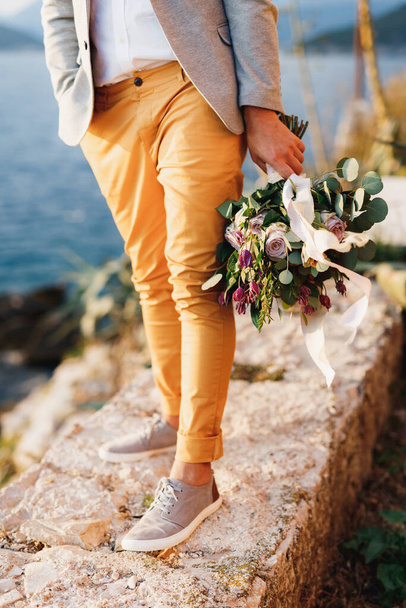 Groom in sneakers with a bouquet of flowers stands on a stone path. Close-up of legs - Photo, Image