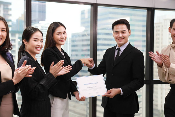 会議室では、アジアの企業チームが支店長に証明書を授与し、残りの従業員は拍手しています - 写真・画像