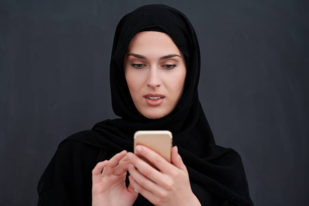 Young muslim businesswoman in traditional clothes or abaya using smartphone - Фото, изображение