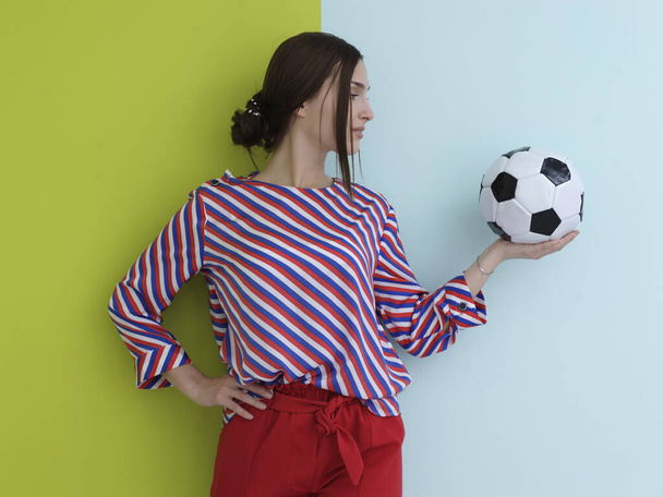 Portrait of young European woman holding soccer ball on her palm. Happy girl, football fan or player isolated on green and blue background. Sport, play football, health, healthy lifestyle concept - Foto, Imagen