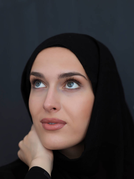 Retrato de una joven musulmana moderna en abaya negra. Chica árabe vestida con ropa tradicional y posando frente a pizarra negra. Representando el estilo de vida árabe moderno y rico - Foto, imagen