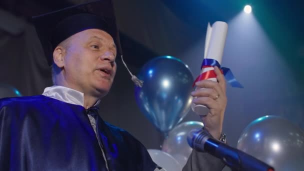 maestro masculino en el manto conduce ceremonia de diploma y felicita alegremente a los estudiantes por la graduación - Metraje, vídeo