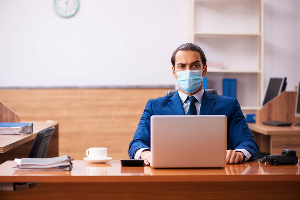 Mladý muž zaměstnanec pracující v kanceláři v masce - Fotografie, Obrázek