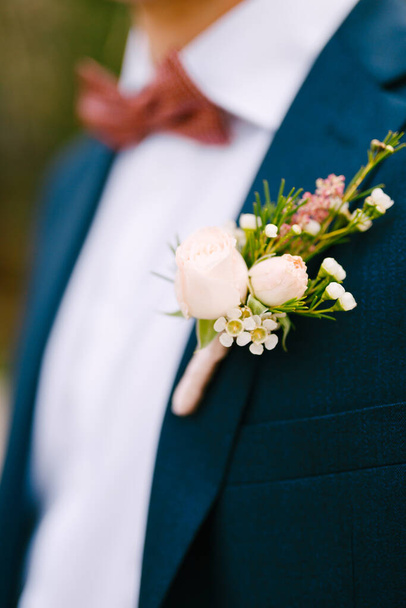 Ένας άντρας με μπλε σακάκι, λευκό πουκάμισο, μπορντό παπιγιόν και μπουτονιέρα με μικρά τριαντάφυλλα και λευκά λουλούδια.  - Φωτογραφία, εικόνα
