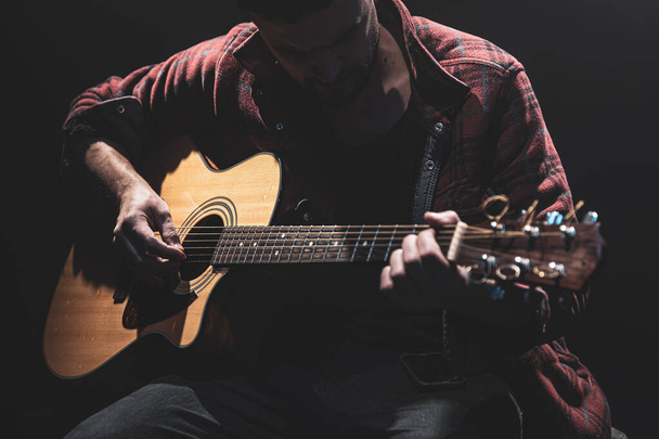 A zenész gitározik, miközben egy sötét szobában ül.. - Fotó, kép