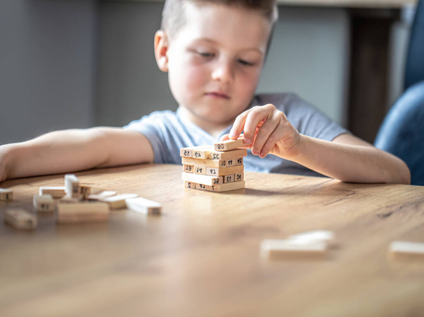 Ein süßer kleiner Junge spielt ein Brettspiel mit Holzwürfeln und einem Turm. - Foto, Bild