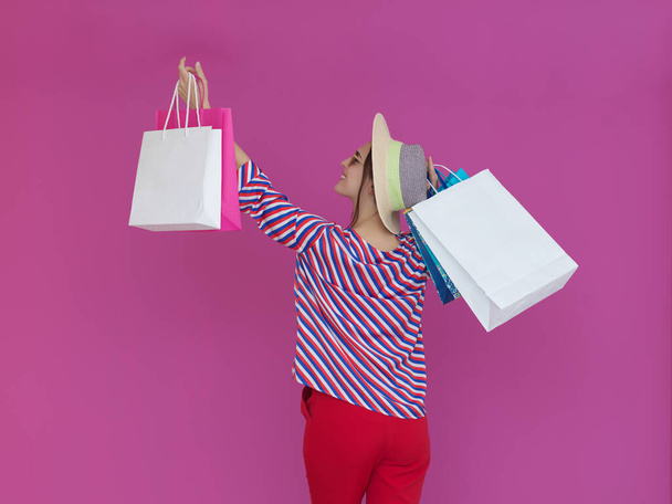Fiatal nő, rózsaszín hátterű bevásárlótáskákkal. Boldog lány pózol új vásárlásokkal egy nap után. Fekete péntek koncepció - Fotó, kép