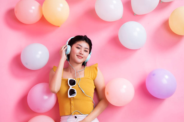 Asian Beauty girl with colorful air balloons laughing over pink background. Young woman on birthday holiday party. Celebrating with pastel color balloon.She listen music and dance. - Foto, afbeelding