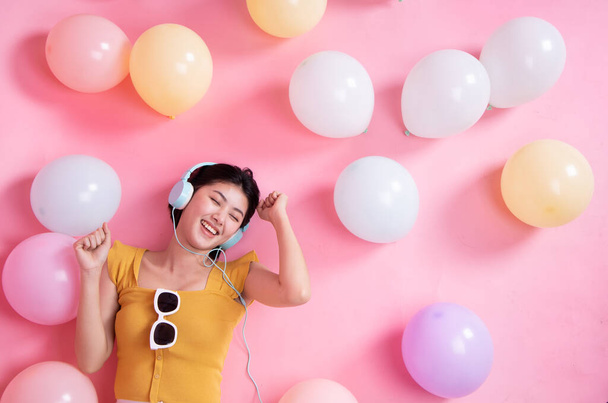 Asian Beauty girl with colorful air balloons laughing over pink background. Young woman on birthday holiday party. Celebrating with pastel color balloon.She listen music and dance. - Photo, image