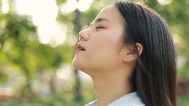 Genç Asyalı kadının yakın plan portresi huzurlu günbatımının keyfini çıkarıyor ve güzel yaz günbatımında halka açık bir parkta dinlenirken temiz hava soluyor.. - Video, Çekim