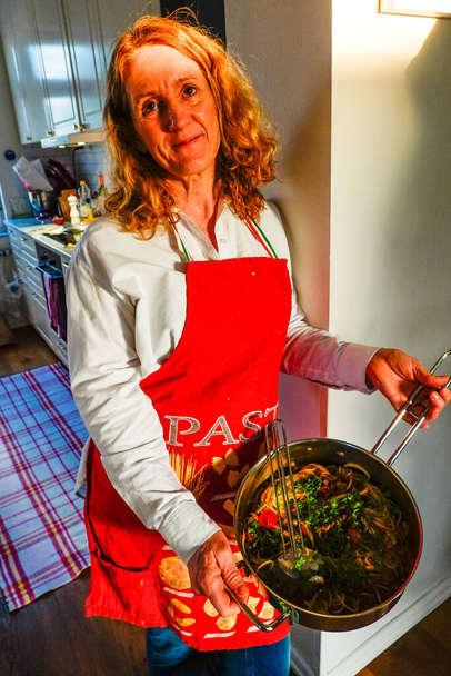 Une femme chef pose dans la cuisine avec tablier et plat de spaghettis. - Photo, image