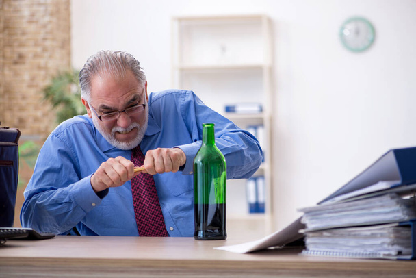 Old male employee drinking alcohol in the office - Foto, Bild