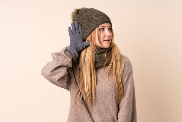 Неповнолітня українська дівчина з зимовим капелюхом ізольована на бежевому фоні, слухаючи щось. - Фото, зображення