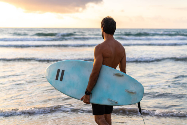 Fiatal fehér férfi korán kel szörfözni napkeltekor. - Fotó, kép