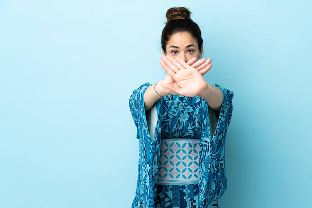Женщина в кимоно на изолированном фоне делает жест остановки рукой, чтобы остановить действие - Фото, изображение
