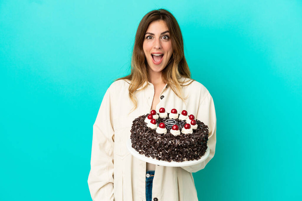 blank vrouw holding verjaardag taart geïsoleerd op blauwe achtergrond met verrassing gezichtsuitdrukking - Foto, afbeelding