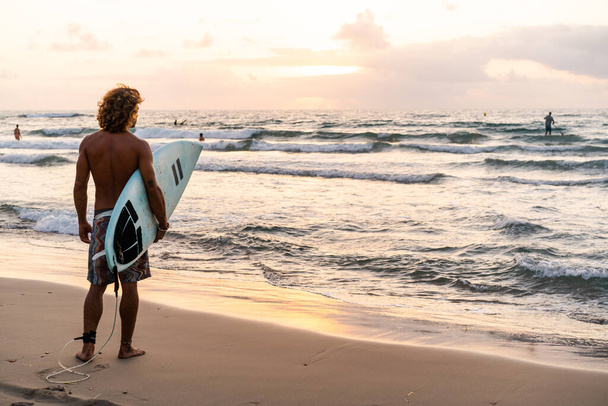 Nuori valkoihoinen mies nousee aikaisin surffaamaan auringonnousun aikaan. - Valokuva, kuva