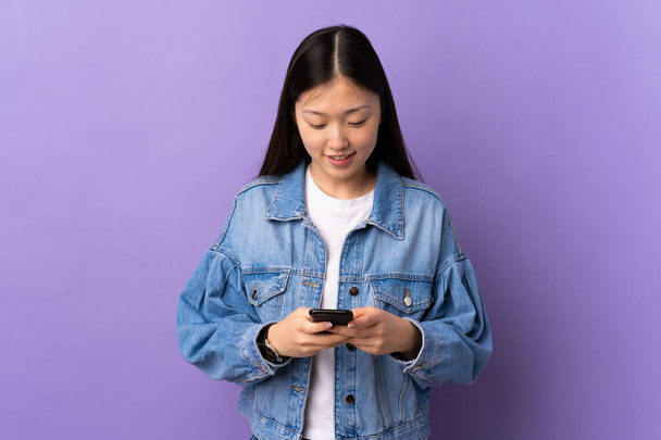 Menina chinesa jovem sobre fundo roxo isolado enviando uma mensagem com o celular - Foto, Imagem