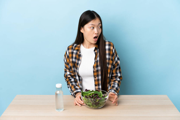 Young Chinese girl eating a salad doing surprise gesture while looking to the side - Foto, Bild