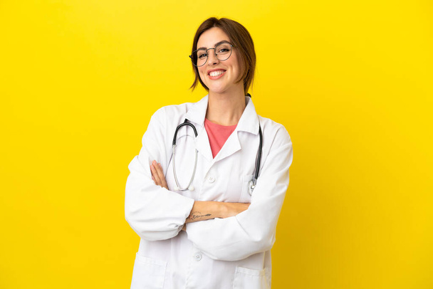 Médica mulher isolada em fundo amarelo mantendo os braços cruzados na posição frontal - Foto, Imagem