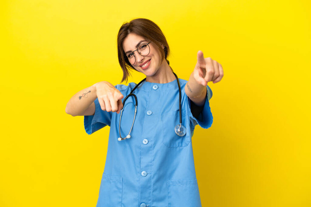 Surgeon doctor woman isolated on yellow background points finger at you while smiling - 写真・画像