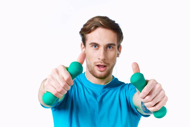hombre deportivo con mancuernas en las manos en los auriculares ejercicio de fitness fondo de luz - Foto, Imagen